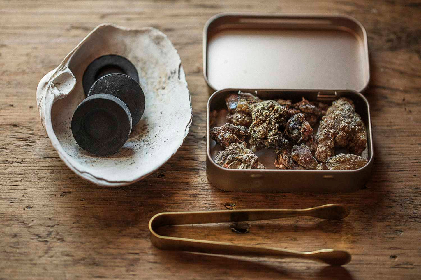 Conifer resin incense kit with charcoal discs in a shell burner, resin in a brass tin, and brass ritual tongs.