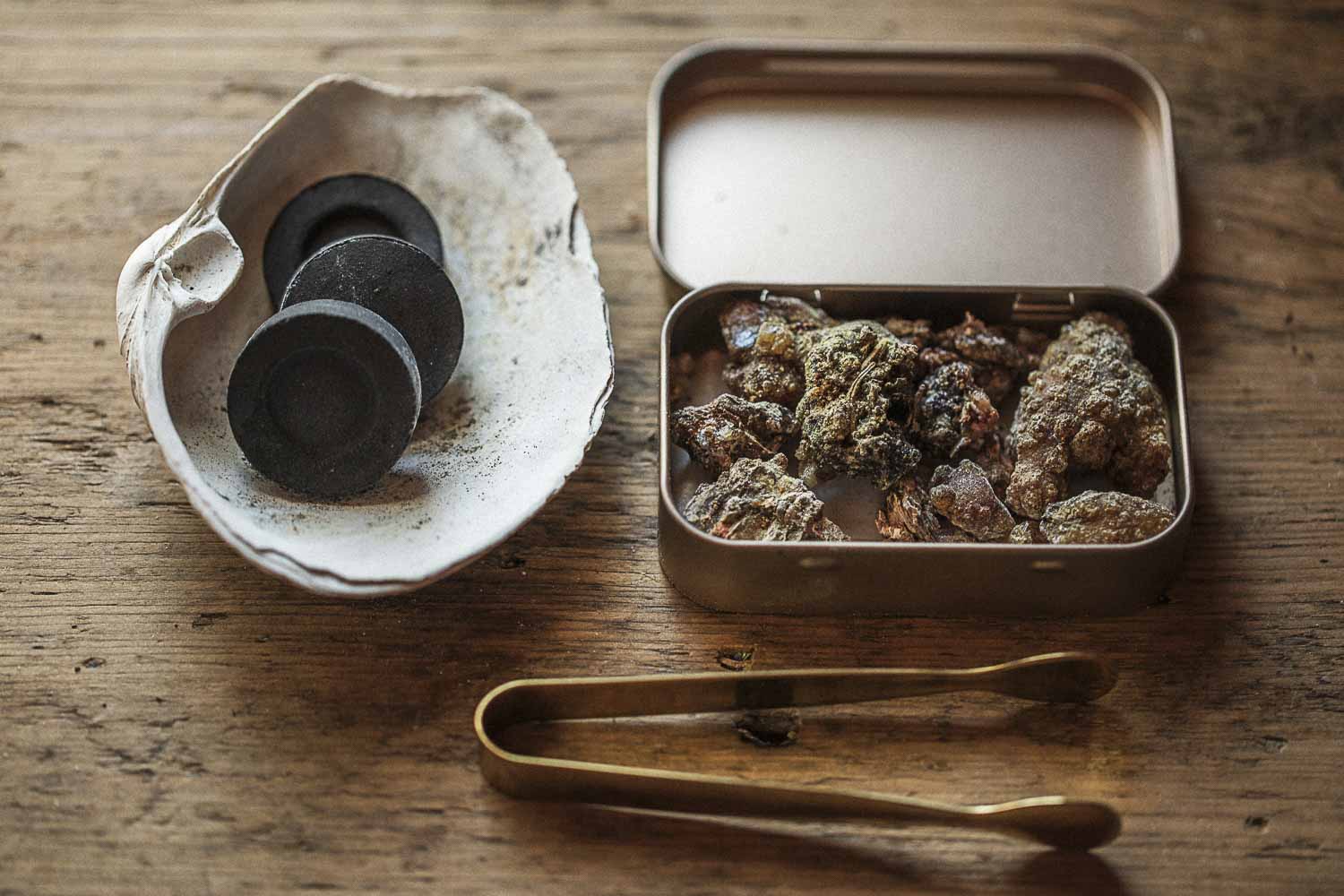 Conifer resin incense kit with charcoal discs in a shell burner, resin in a brass tin, and brass ritual tongs.