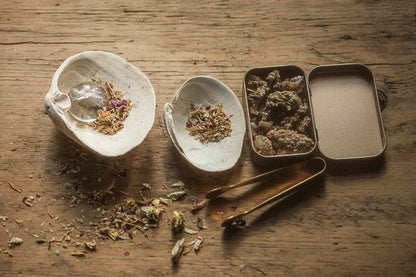 Shell burner with dried herbs, conifer resin  in rose gold tin on a wooden surface
