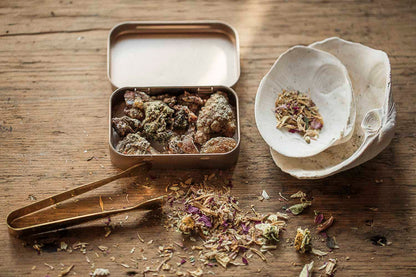 Natural conifer resin incense with shell burner, brass tongs, and botanicals arranged on a wooden ritual table.