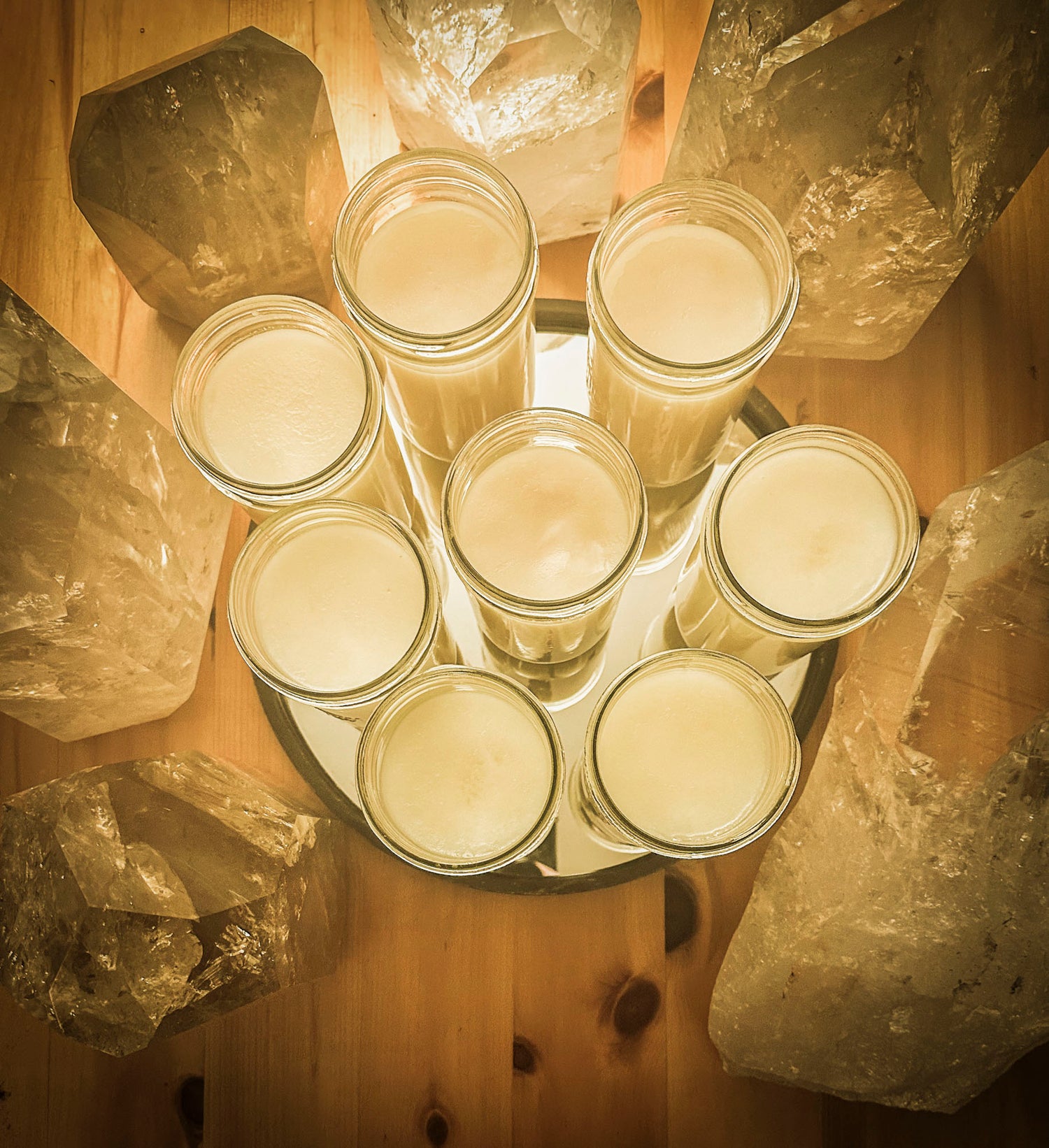 WYLDE GOLD tallow jars arranged on mirrored tray, surrounded by quartz crystals on pinewood surface