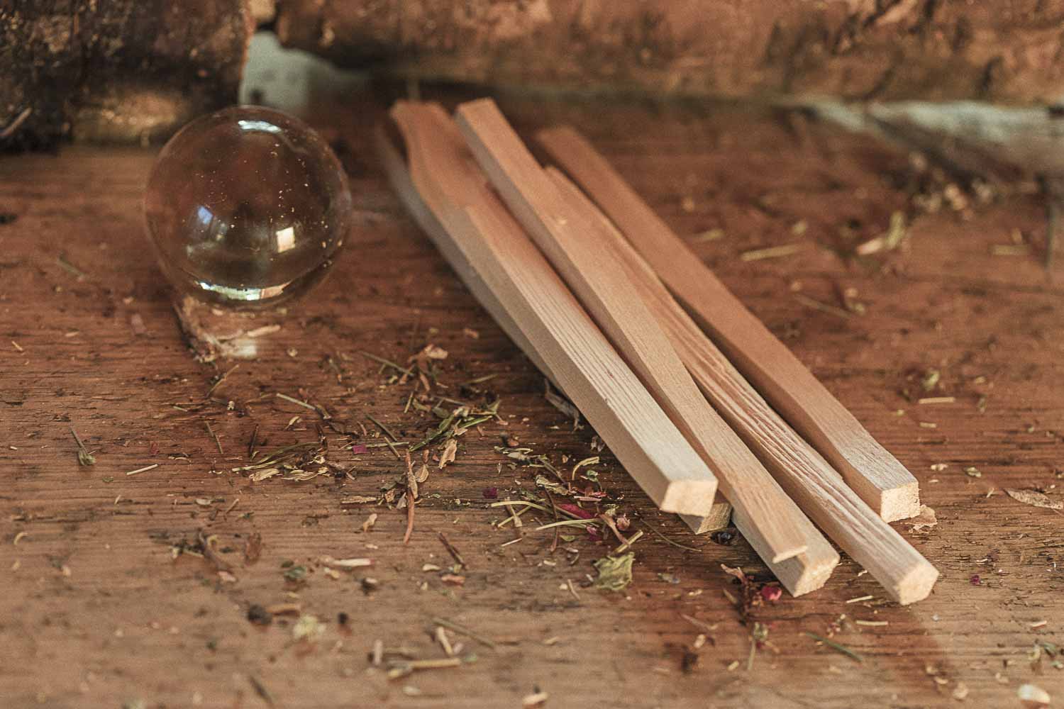 Three wooden sticks on a rustic wooden surface with a clear quartz orb and dried herbs.