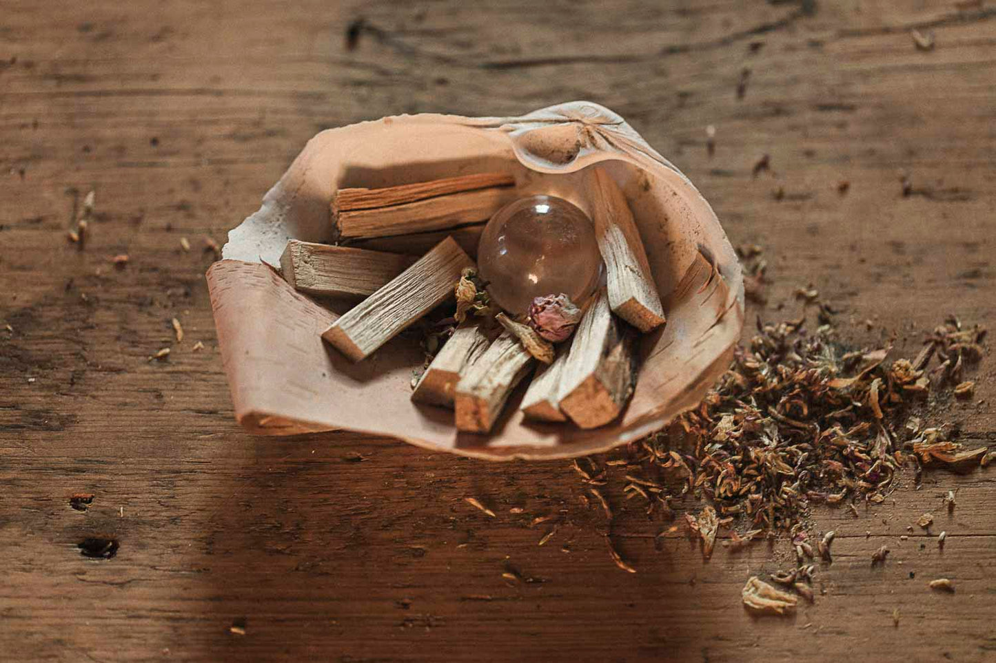 Clam shell holding a crystal ball with wooden sticks and dried herbs on a wooden surface