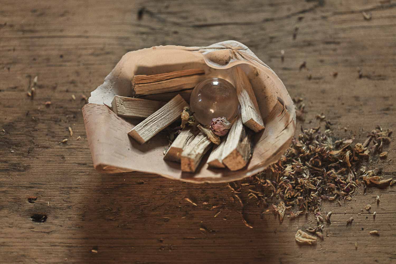 Clam shell holding a crystal ball with wooden sticks and dried herbs on a wooden surface