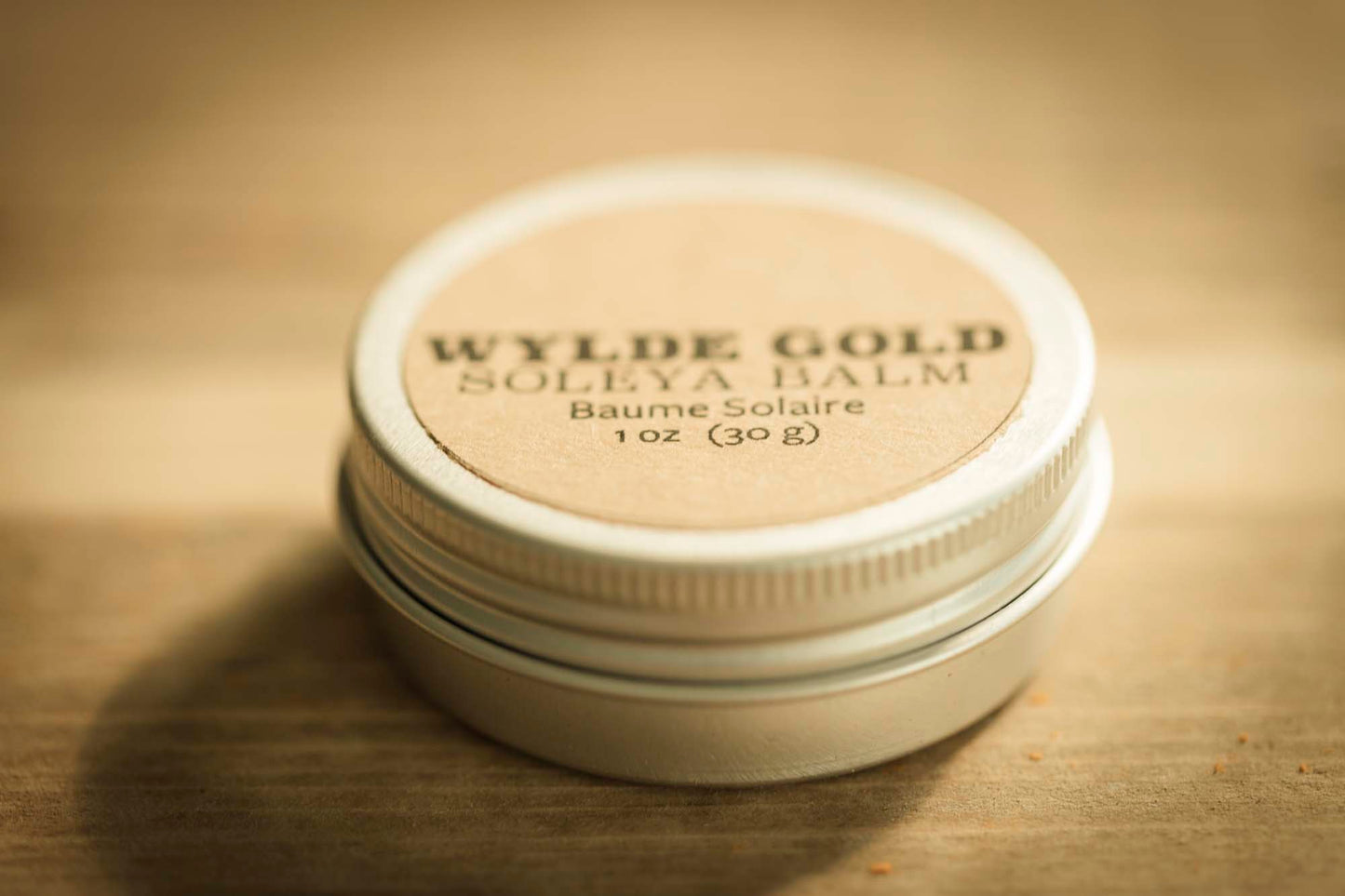 WYLDE GOLD Soleya Balm tin on rustic wood background – 1 oz sun balm with SPF, natural kraft label and metal lid.