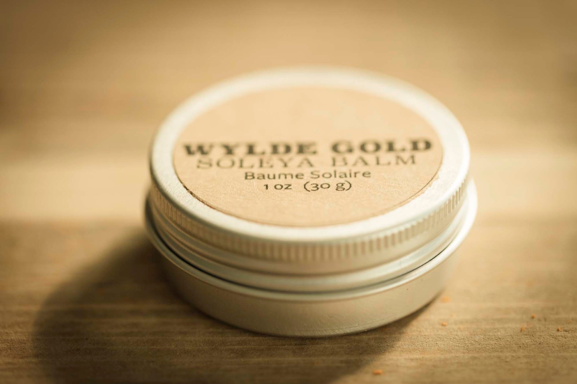 WYLDE GOLD Soleya Balm tin on rustic wood background – 1 oz sun balm with SPF, natural kraft label and metal lid.