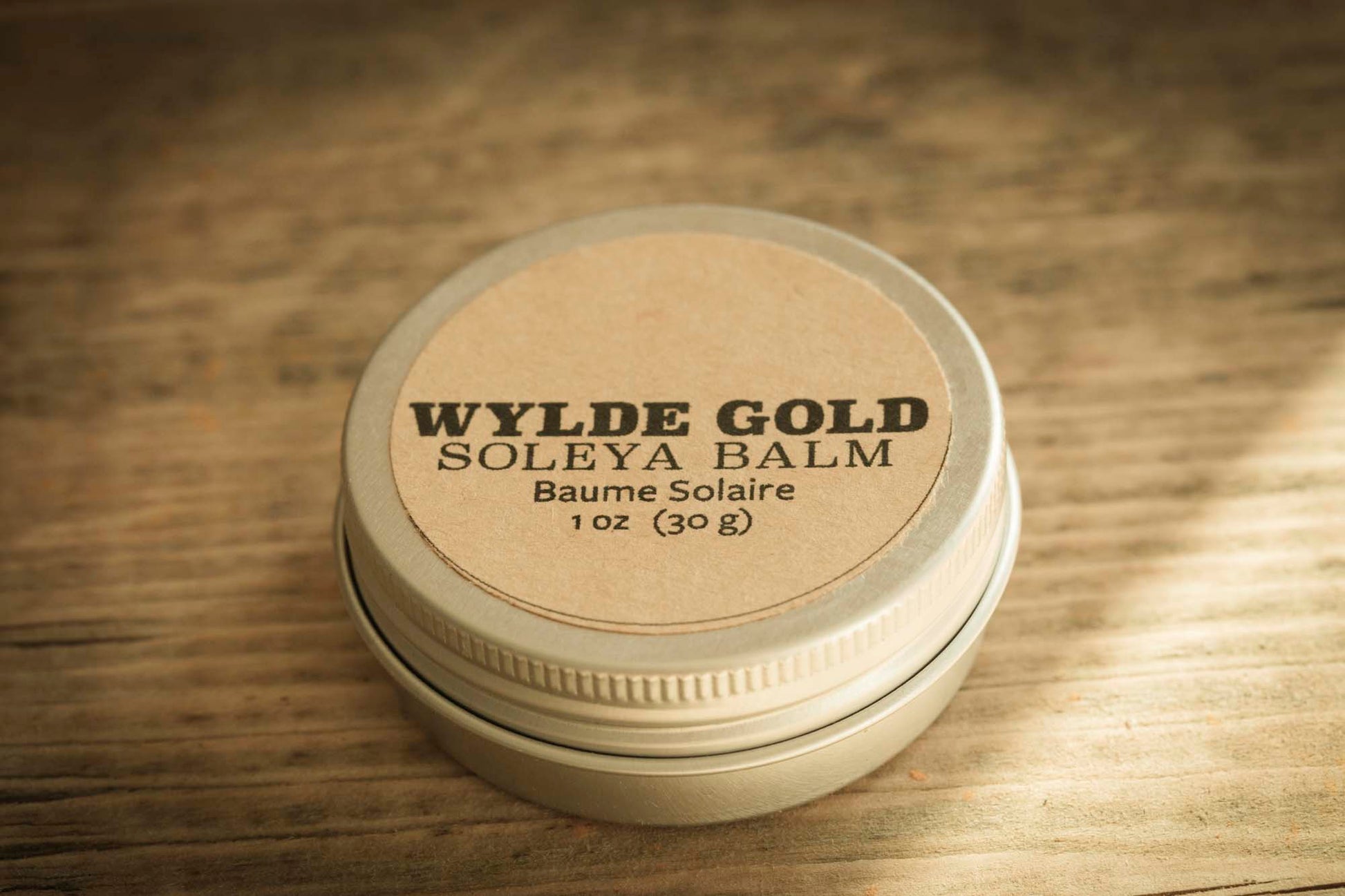 WYLDE GOLD Soleya Balm tin on rustic wood background – 1 oz sun balm with SPF, natural kraft label and metal lid.