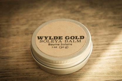 WYLDE GOLD Soleya Balm tin on rustic wood background – 1 oz sun balm with SPF, natural kraft label and metal lid.