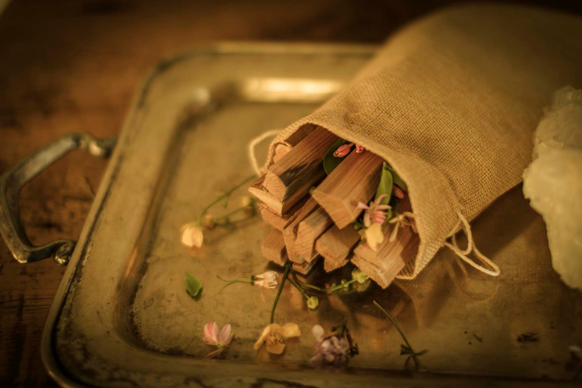 WYLDE GOLD Burlap pouch of cedar smudge sticks and wildflowers and quartz on silver ritual platter with soft golden lighting