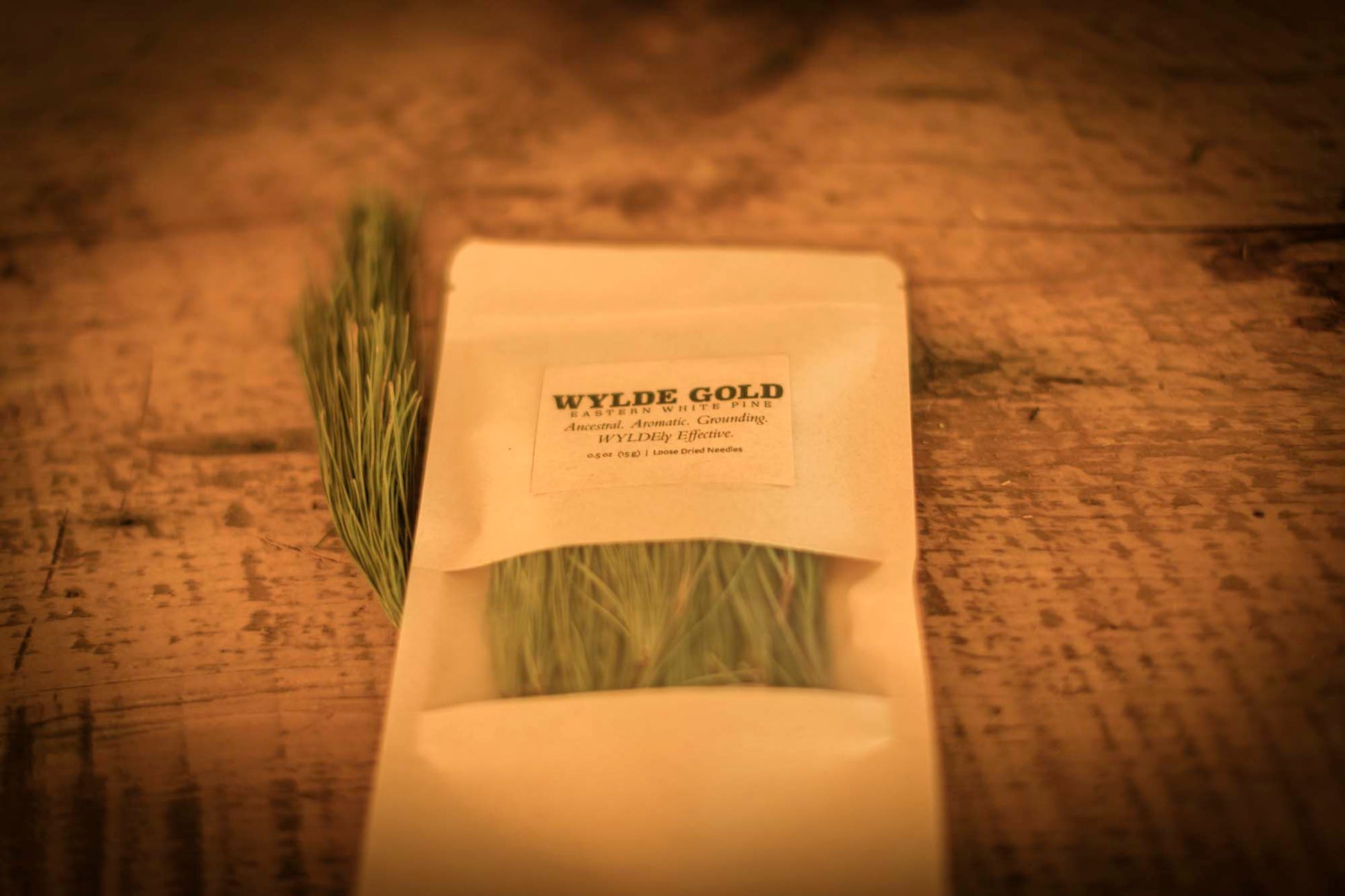 WYLDE GOLD Anoint the Pine — pouch of loose dried pine needles on rustic wood table with fresh pine sprig