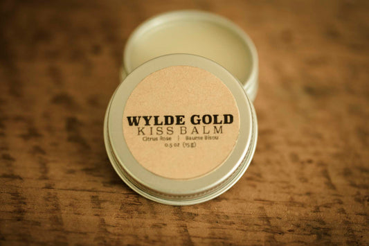 WYLDE GOLD Kiss Balm — Citrus Rose scented grass-fed tallow lip ritual in an open tin on wood