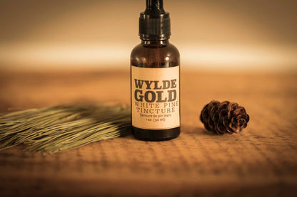 WYLDE GOLD White Pine Tincture — amber dropper bottle on rustic wood with pine sprig & cone