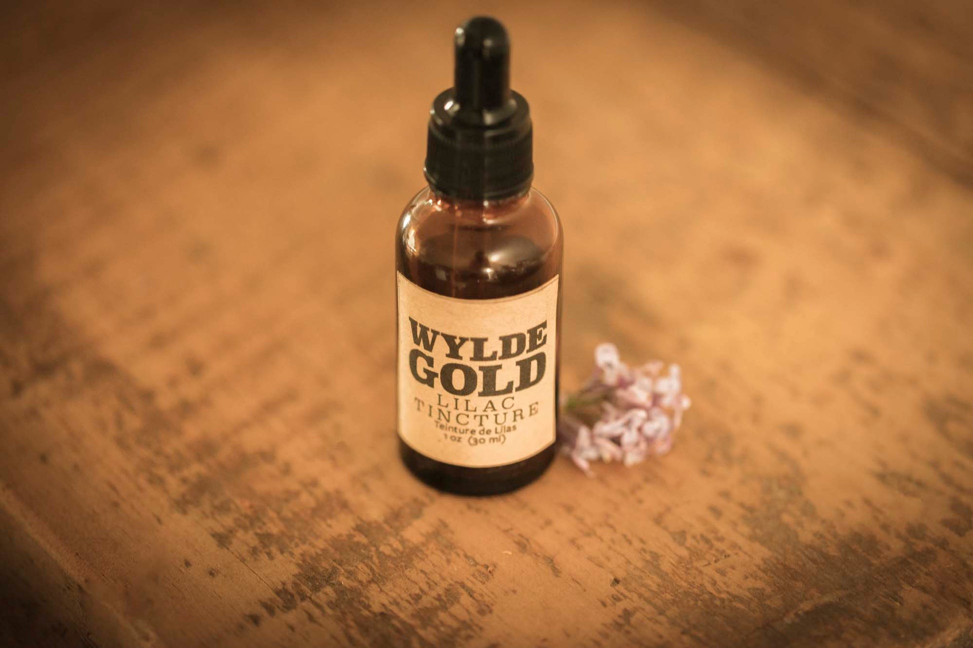 WYLDE GOLD Lilac Tincture — amber dropper bottle on rustic wood with fresh lilac flower