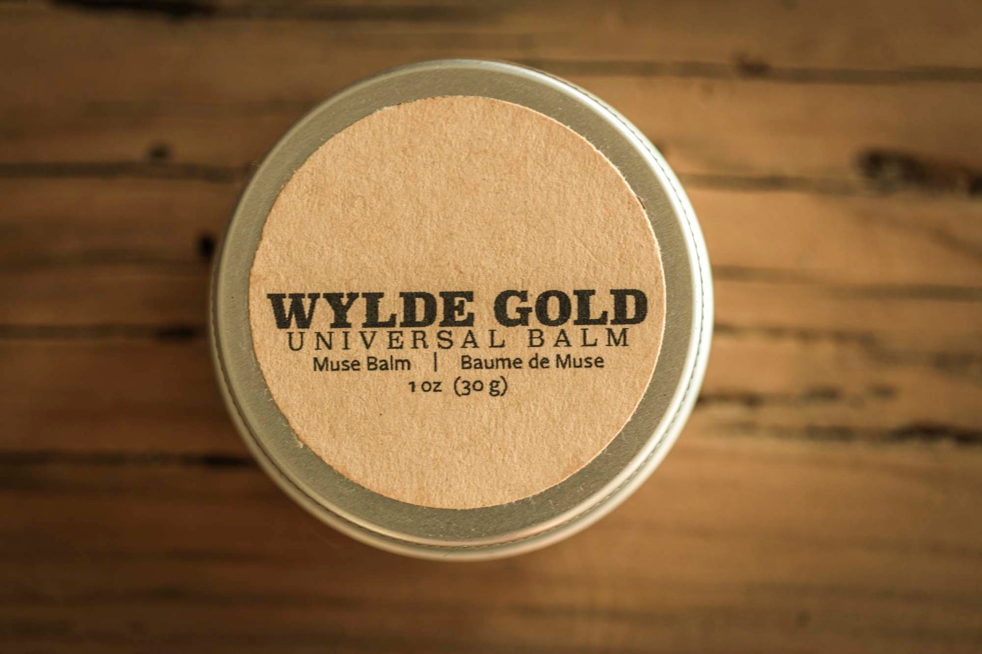 Wylde Gold Universal balm tin container on a rustic wooden background.