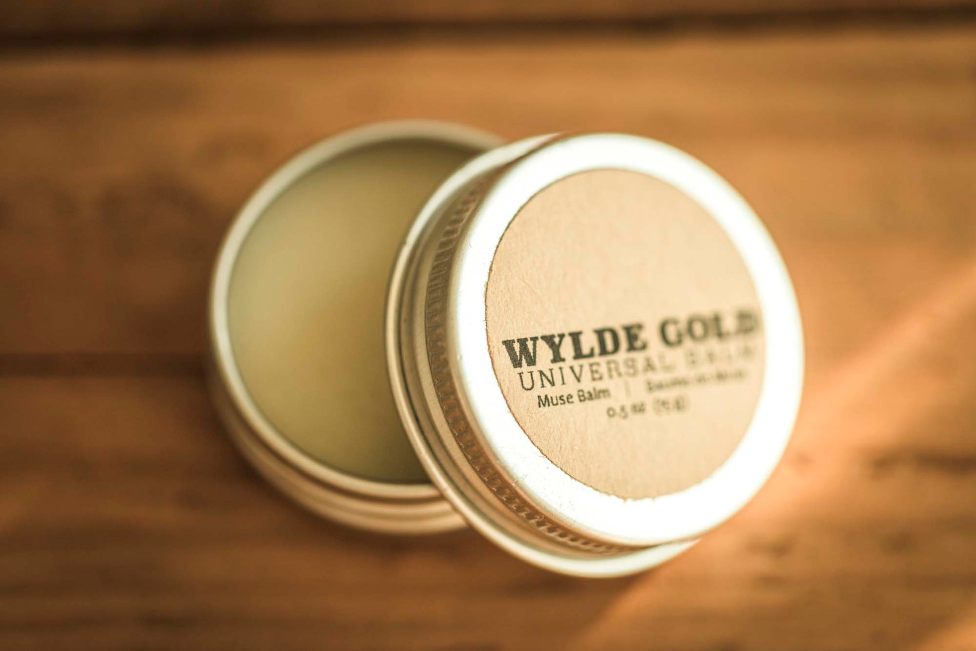 Wylde Gold Universal balm in a tin container on a rustic wooden background.
