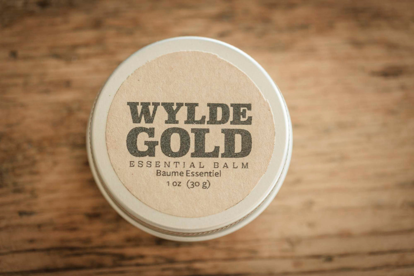 Wylde Gold essential balm container on a wooden surface