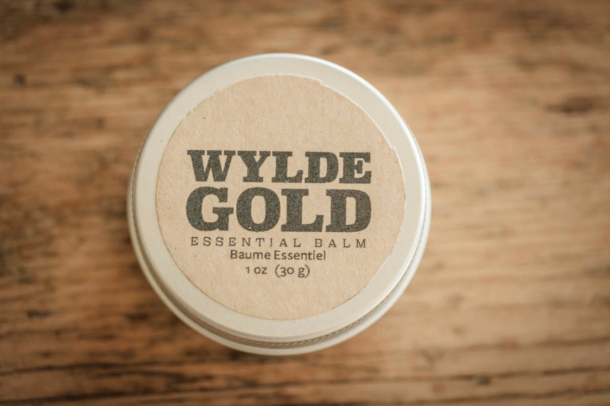 Wylde Gold essential balm container on a wooden surface