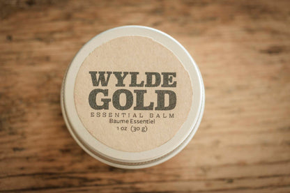 Wylde Gold essential balm container on a wooden surface