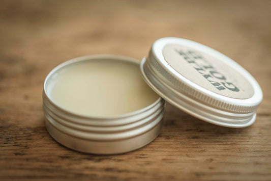 Open Essential Balm tin with lid resting beside it, showing smooth balm surface on a rustic wood table.